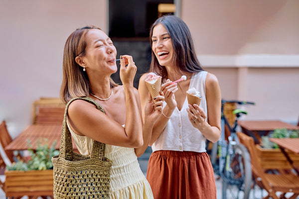 two women sharing an ice cream together, joyfully laughing and smiling together, enjoying their cherished friendship